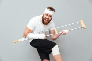 Cheerful playful young man having fun with crutch