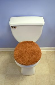 A modern looking toilet with a fuzzy, orange toilet seat cover.